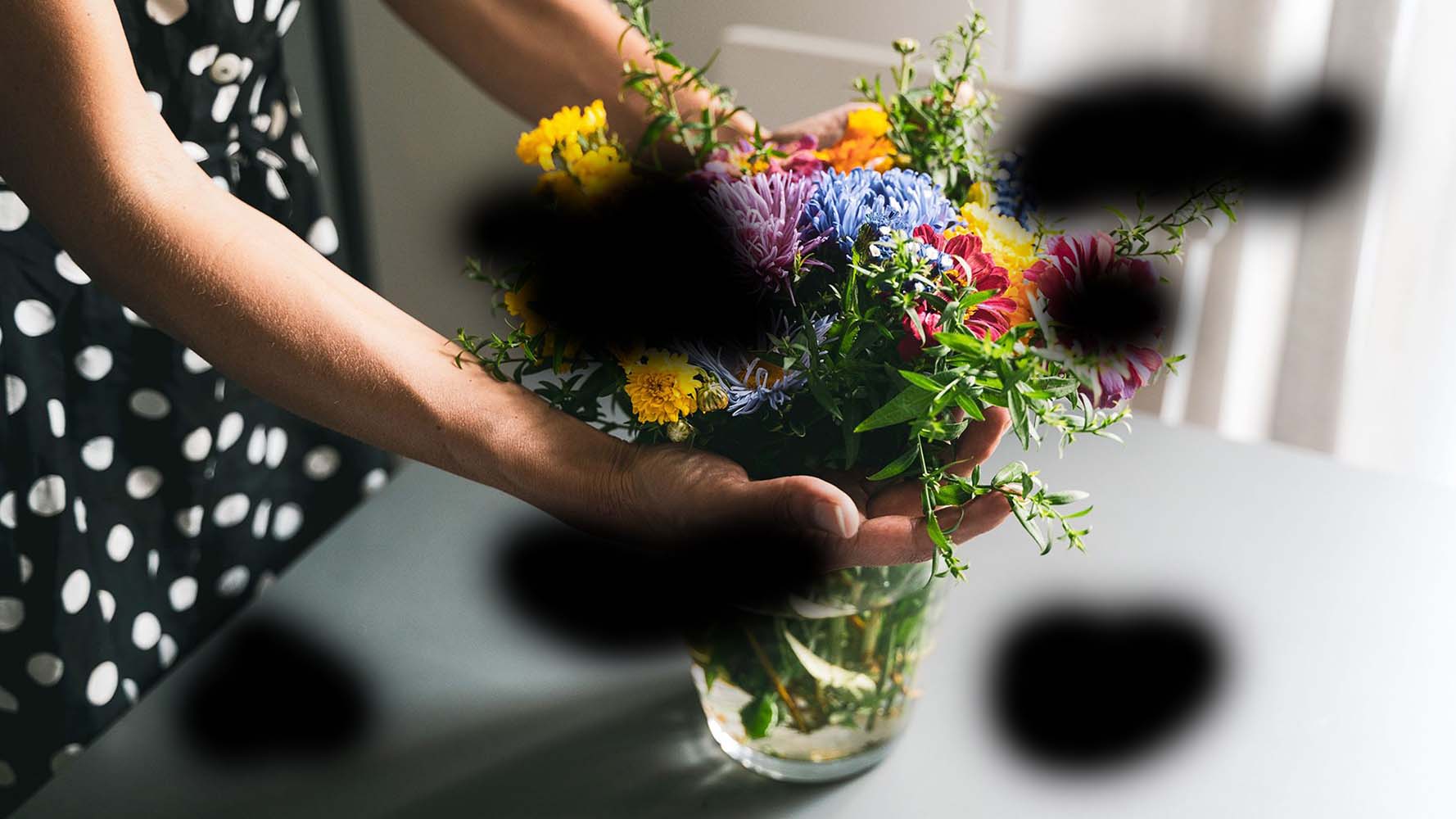 Hands holding flowers, with areas of black blotches obstructing the image, to indicate what a person with diabetic retinopathy might experience.